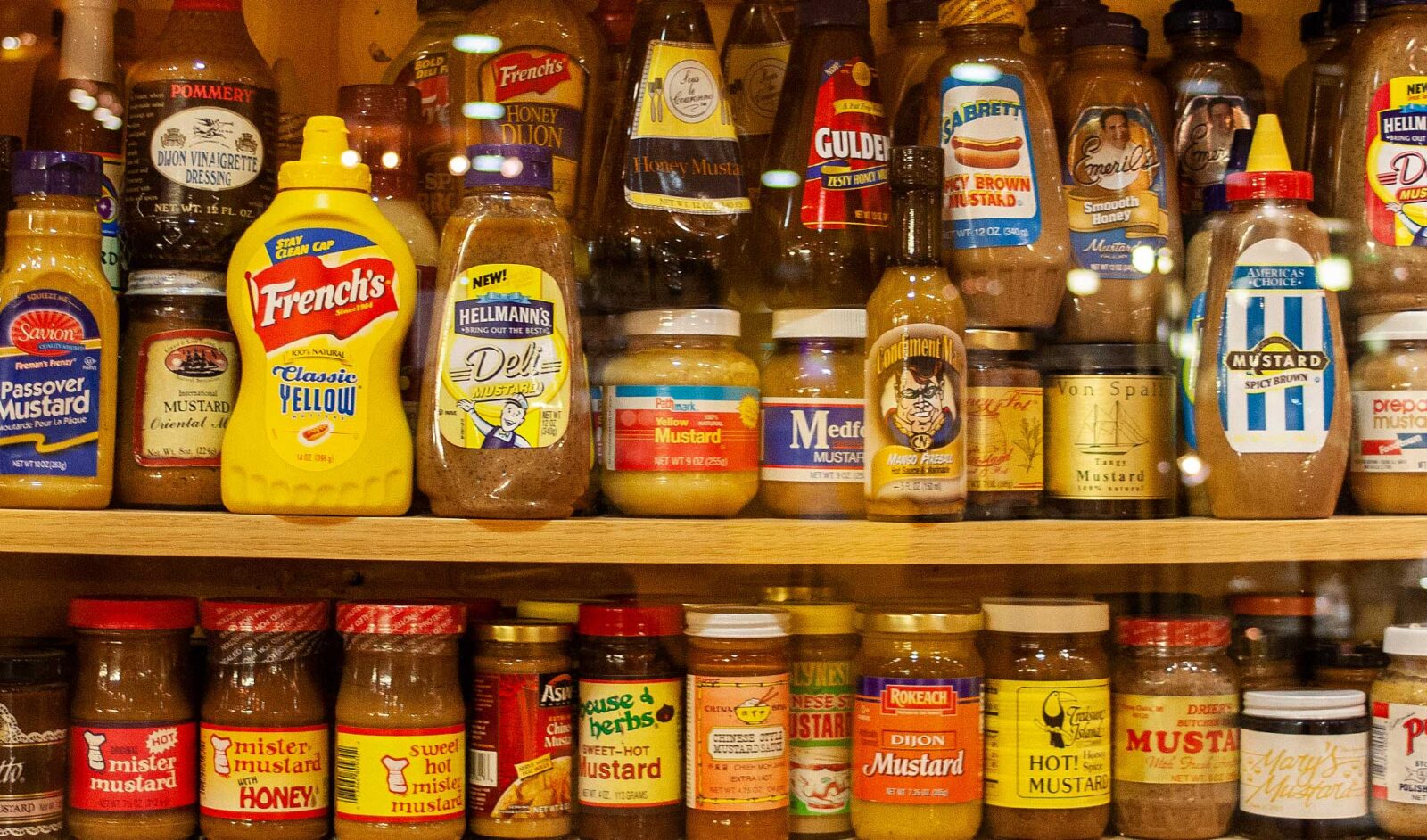 Many different kinds of jars of mustard on shelves